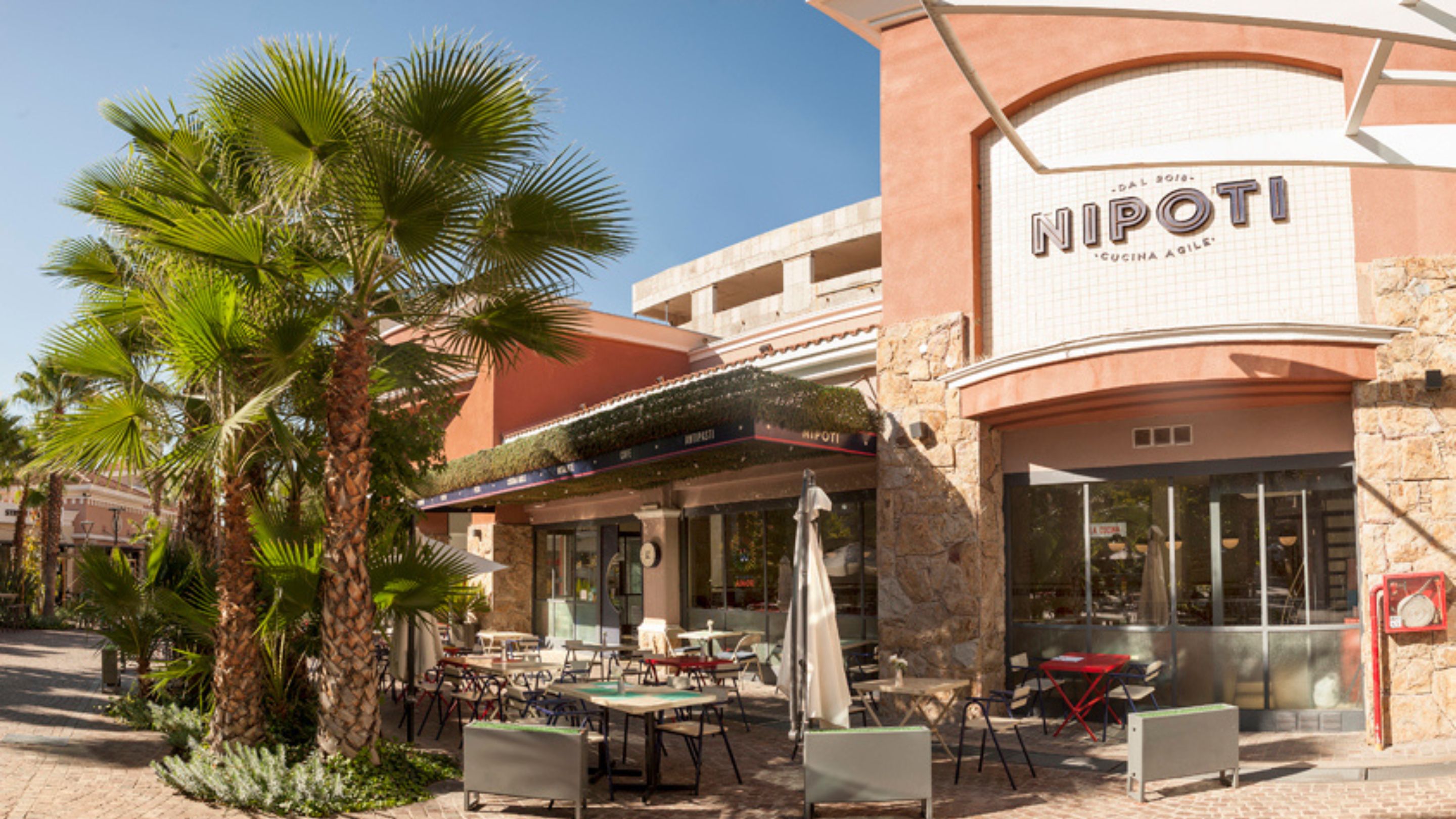 Frente de Nipoti en Palmares Open Mall, con mesas al aire libre y palmeras